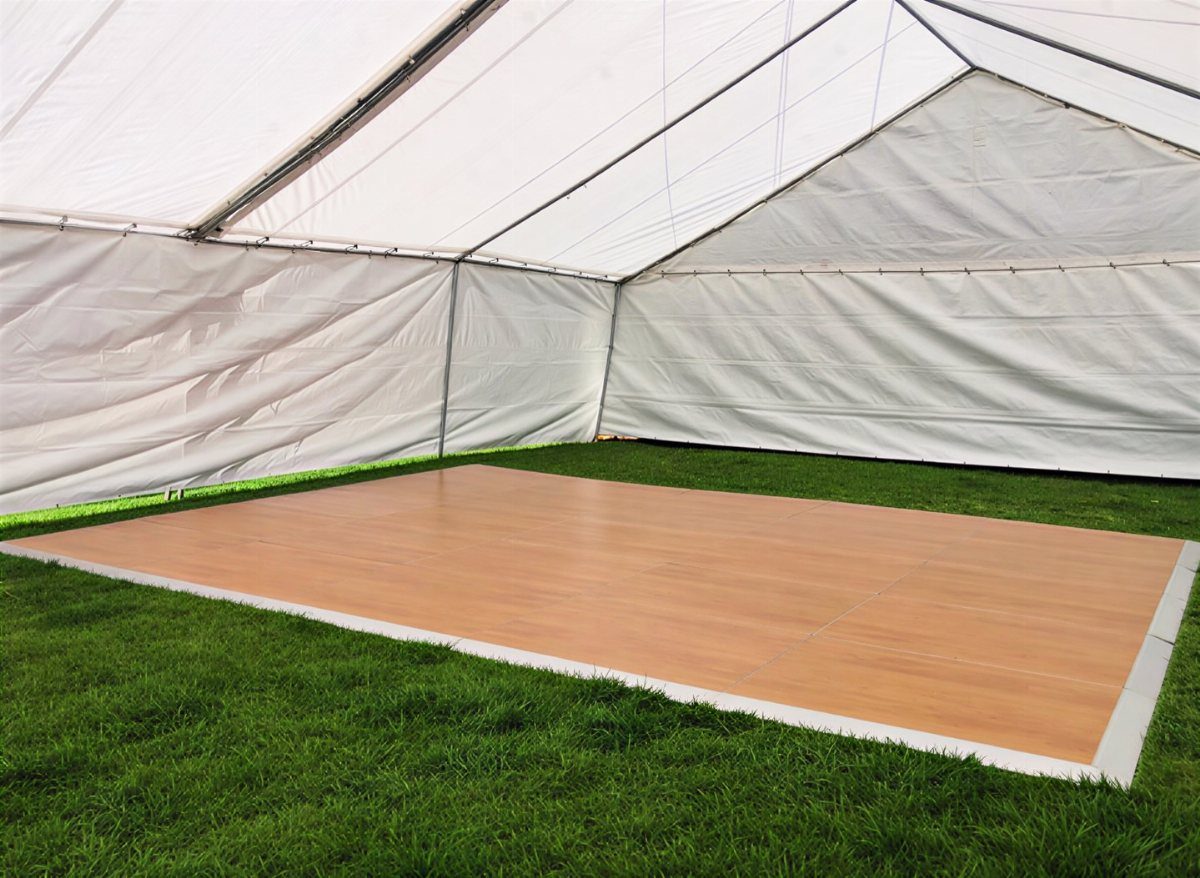 Wooden dance floor installed on green grass inside a white event tent.