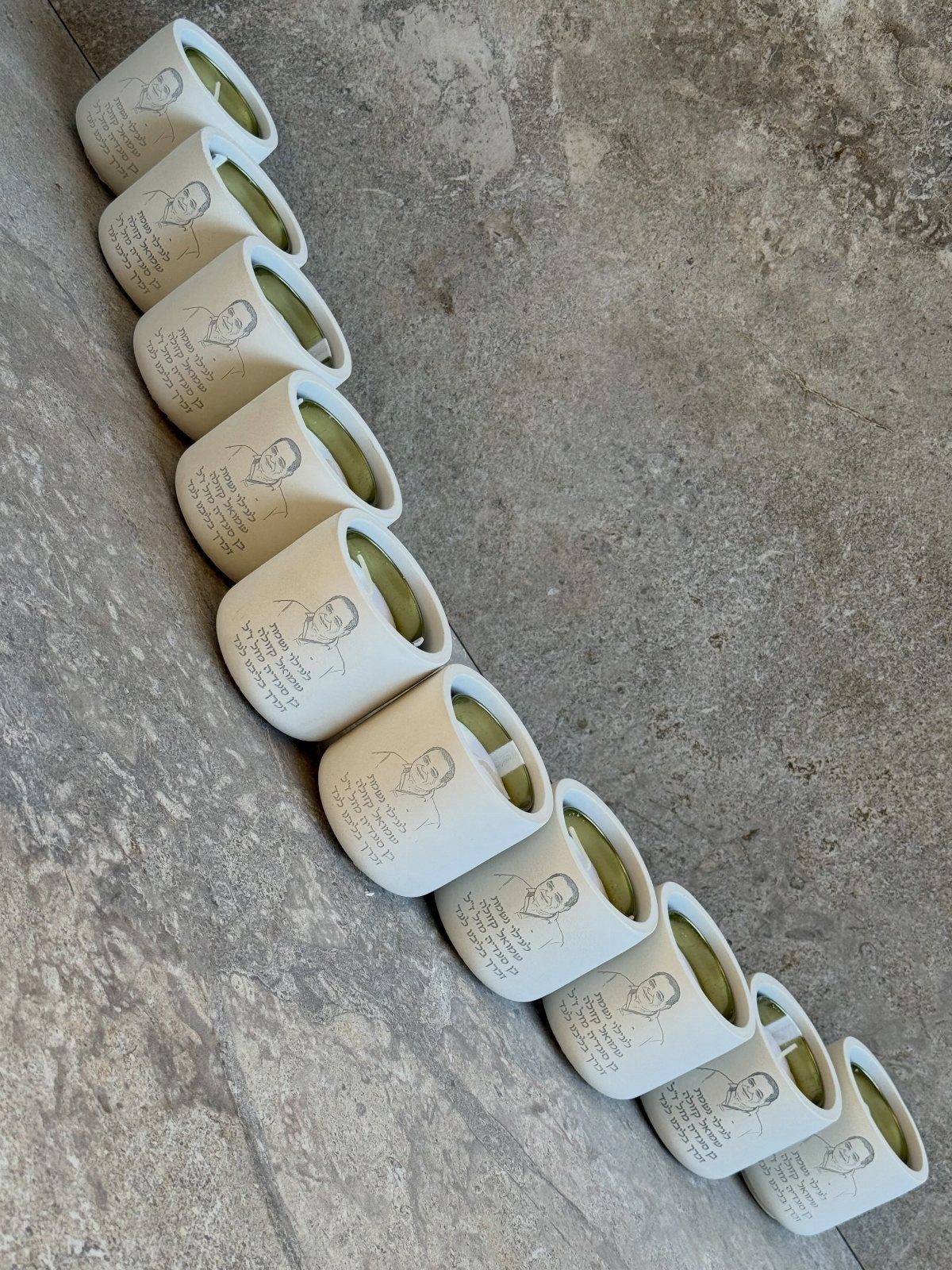 Thirteen personalized white candles with photos arranged in a curve on stone.