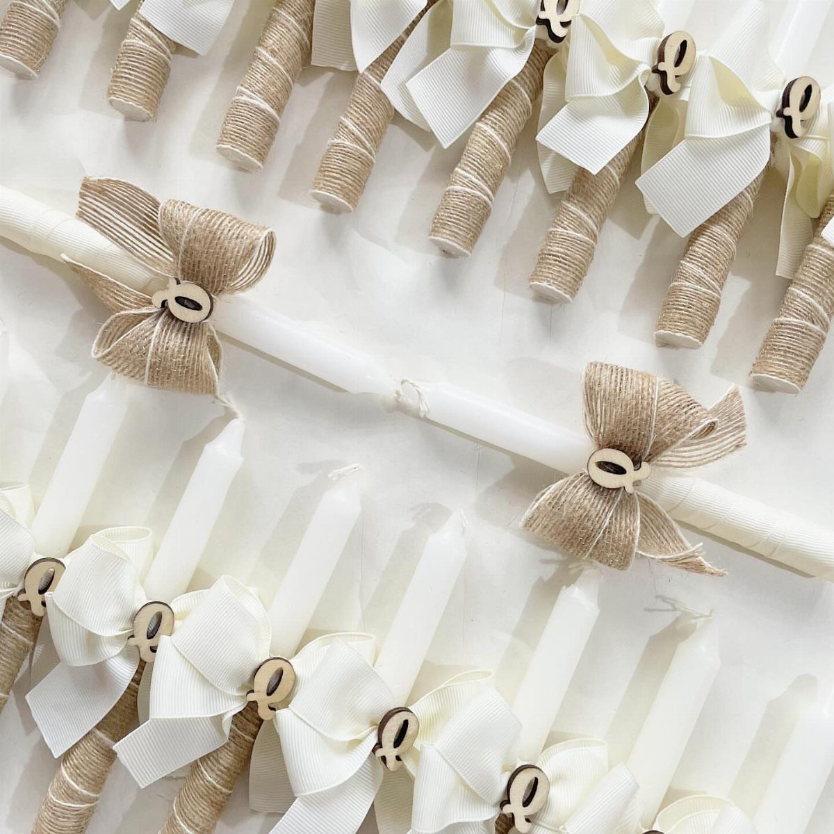 White candles decorated with burlap ribbons, twine wraps, and small circular charms.