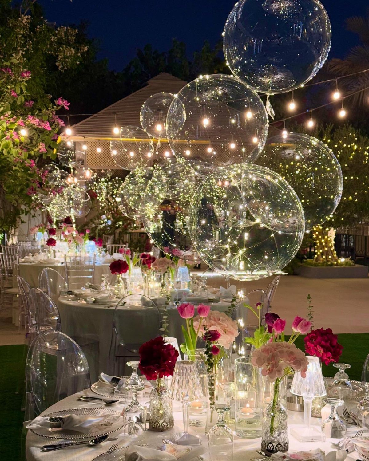 Clear balloons filled with glowing fairy lights floating over elegant floral table centerpieces.