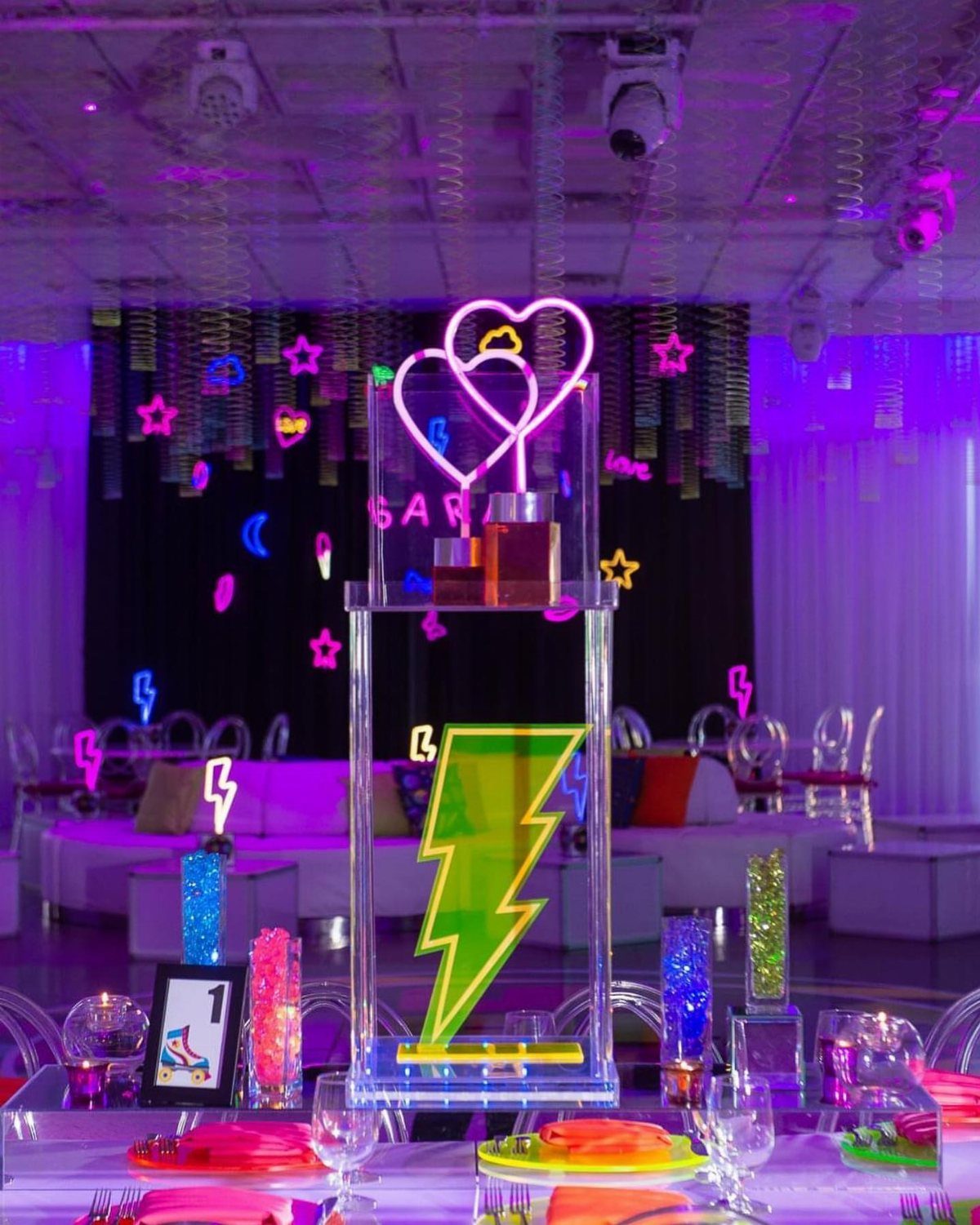Neon heart and lightning bolt acrylic centerpiece on a purple-lit event table.