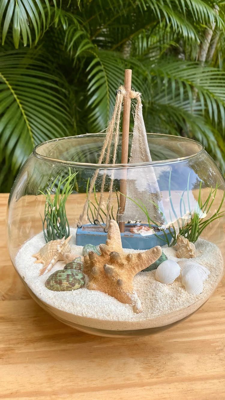 Glass bowl centerpiece with white sand, starfish, seashells, and a miniature sailboat.
