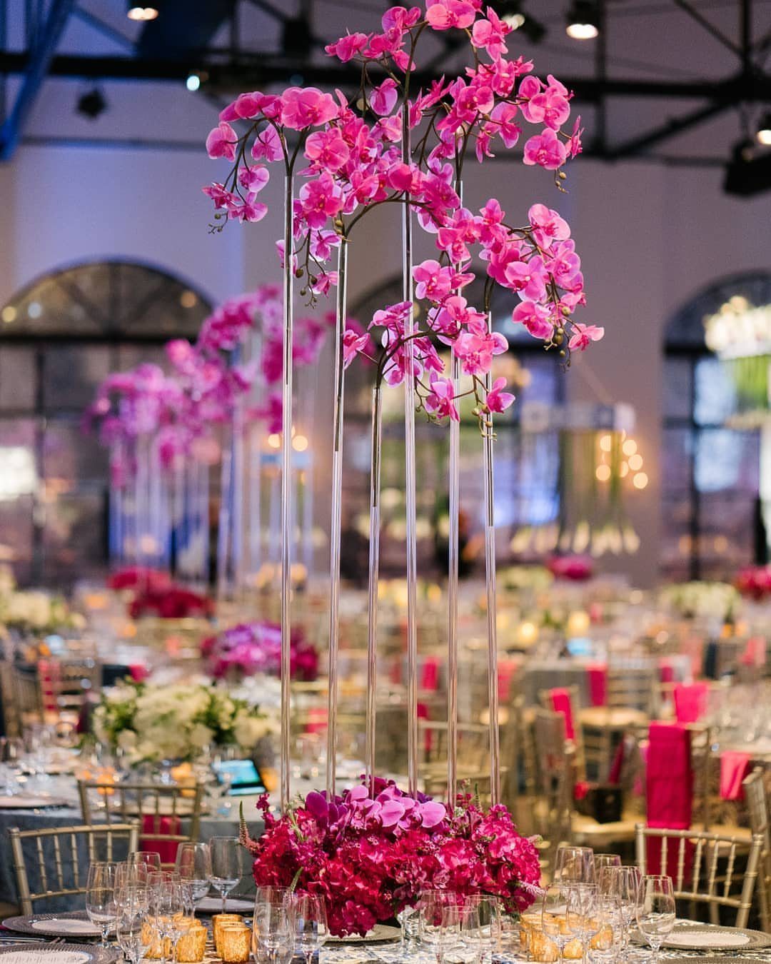 Tall acrylic tube centerpieces with pink orchids in a formal banquet hall setting.