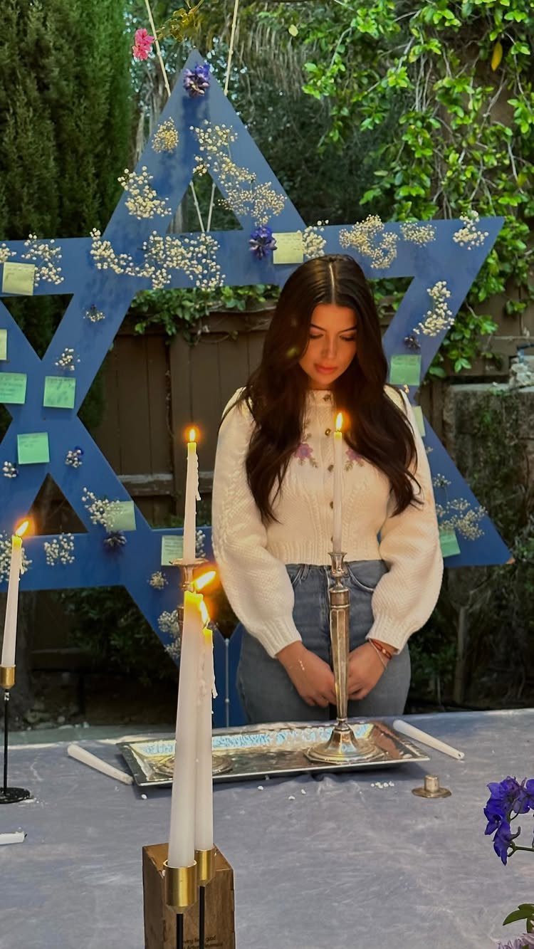 Young woman lighting candles in front of a large blue Star of David decoration.
