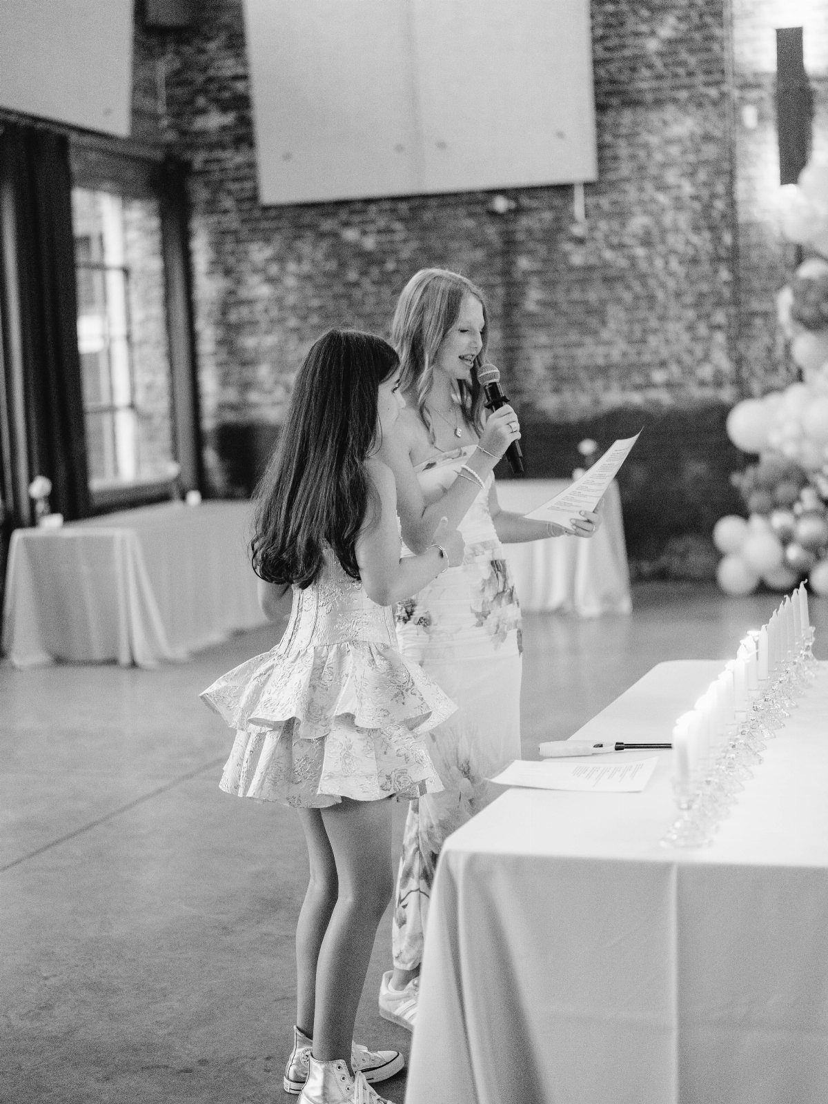 Two girls standing by a table with a row of small white candles.