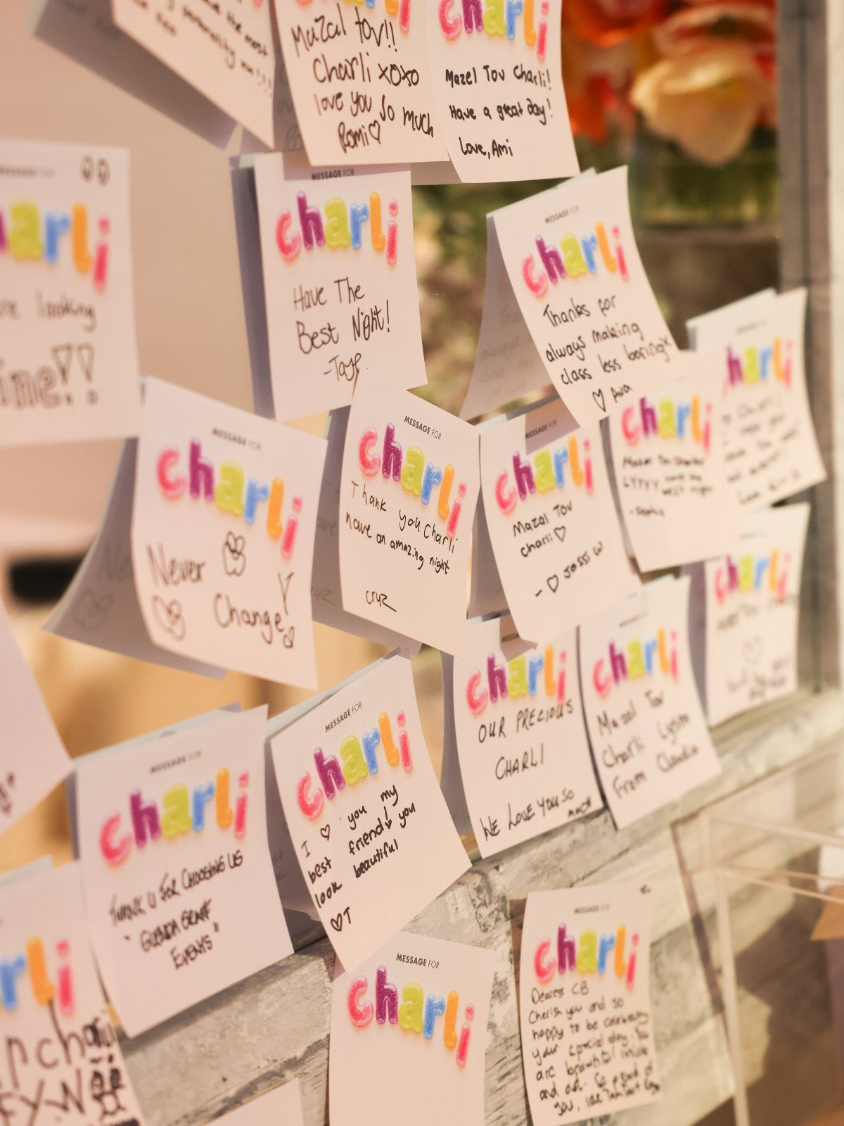 Handwritten Mazel Tov cards for Charli pinned to a wall with colorful lettering.