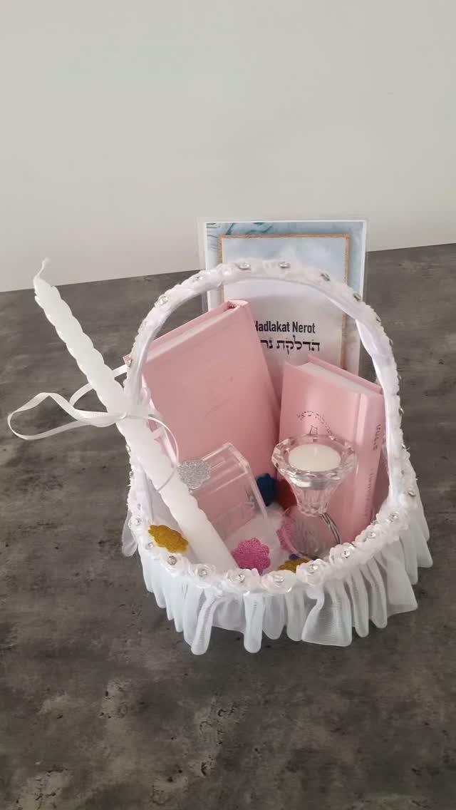 White decorative gift basket with pink books and candles on a grey surface