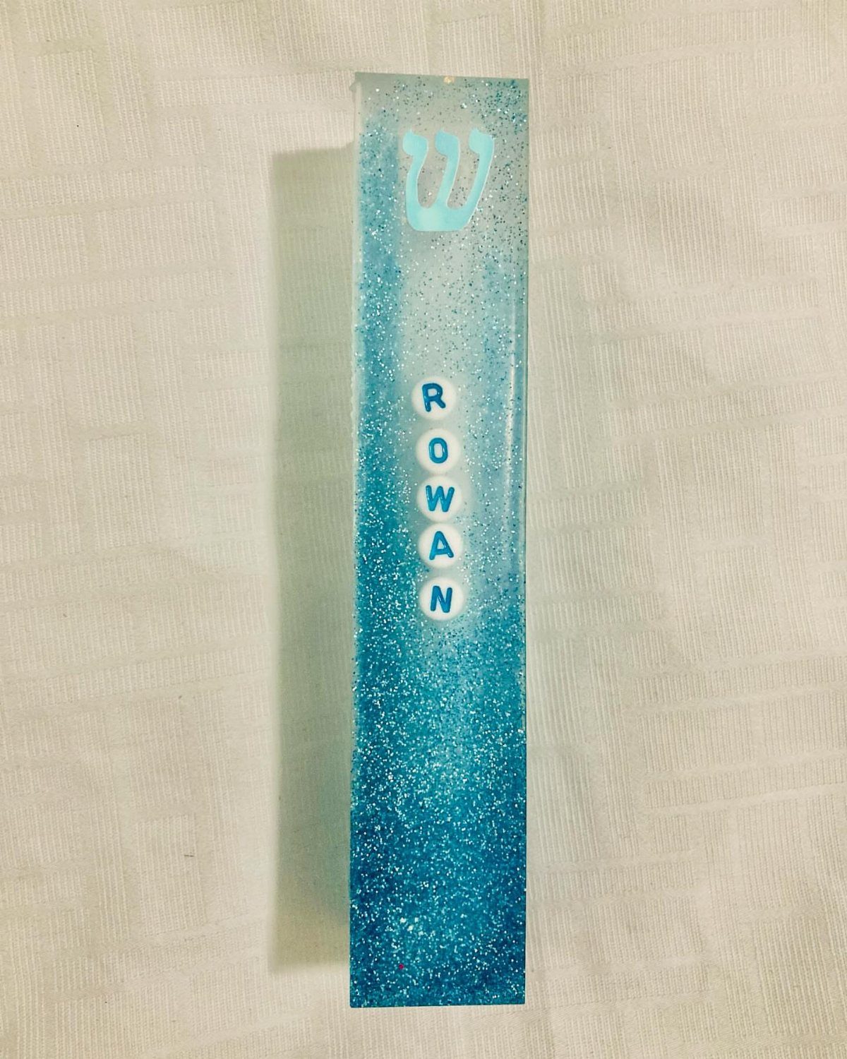 Blue glittery resin block with Hebrew letter Shin and name Rowan in beads.