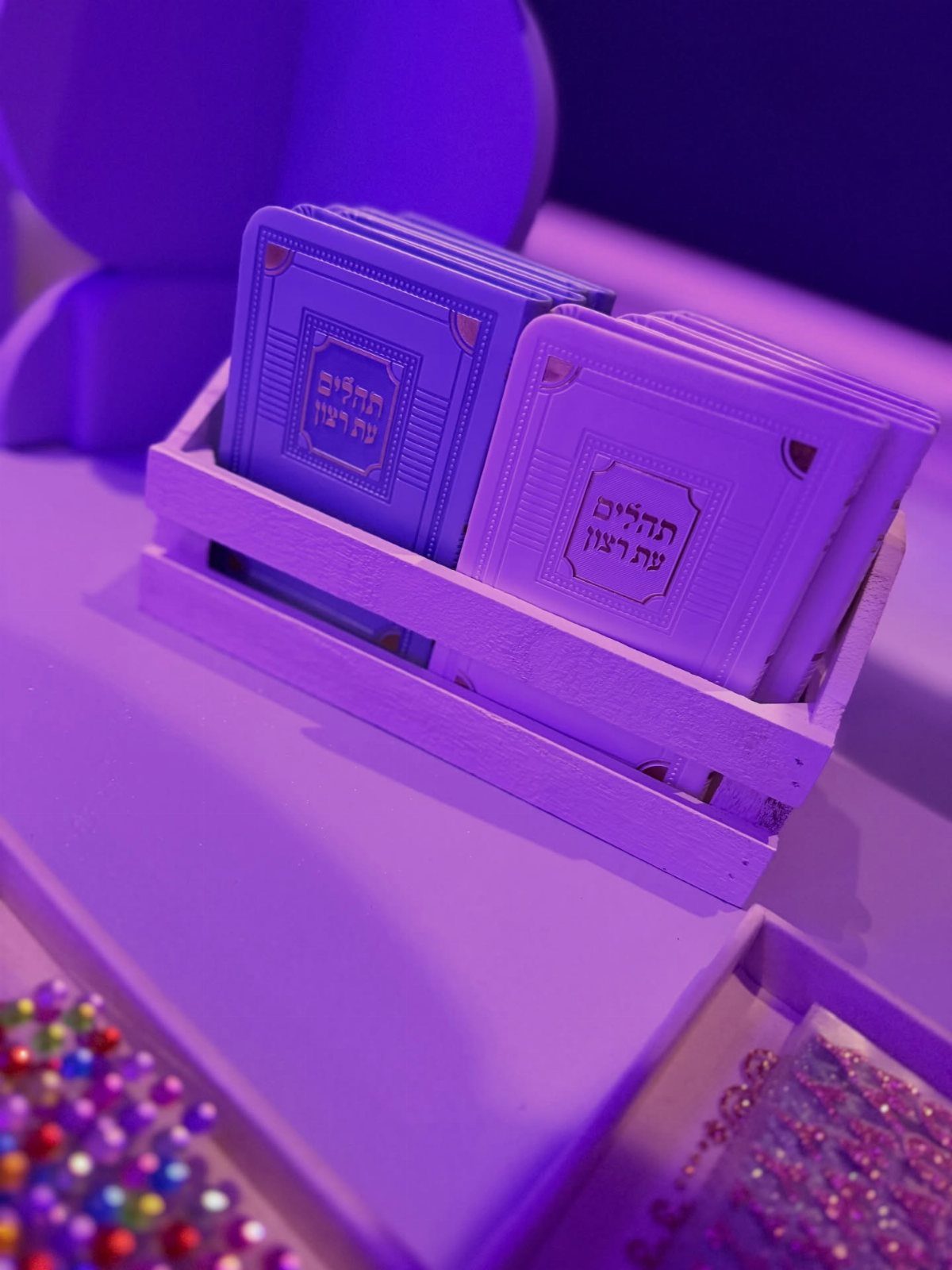 Blue and white Hebrew prayer books in a wooden crate under purple light