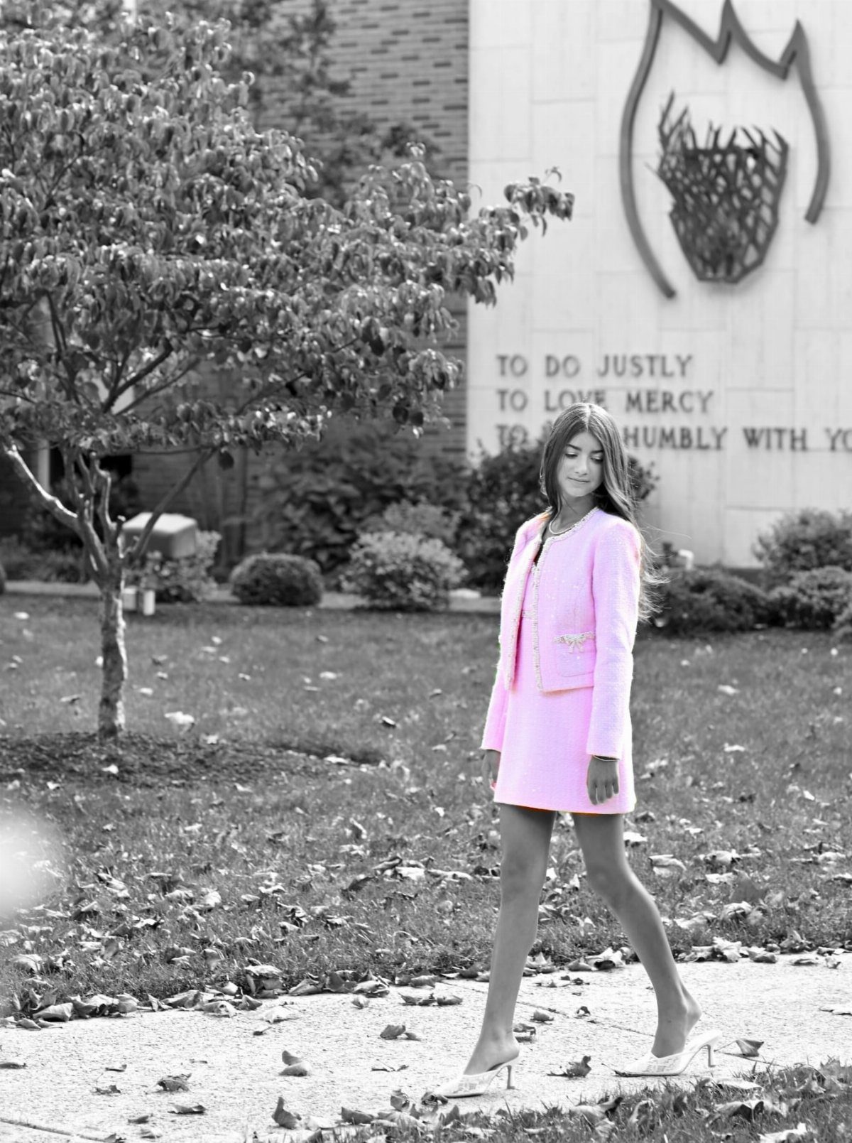 Woman wearing a bright pink short skirt suit and white high heels walking outdoors.