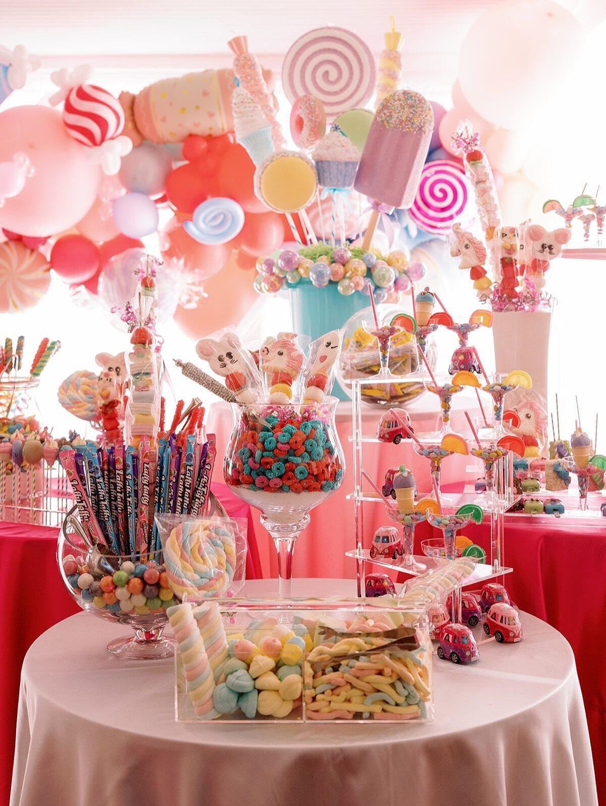 Candy buffet with colorful sweets, lollipops, and balloons on a white table.