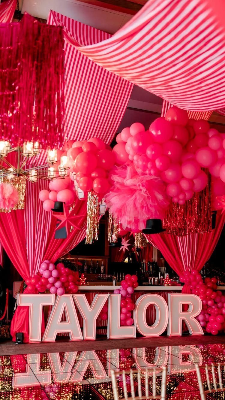Pink and red party decor with large illuminated letters spelling TAYLOR on reflective floor