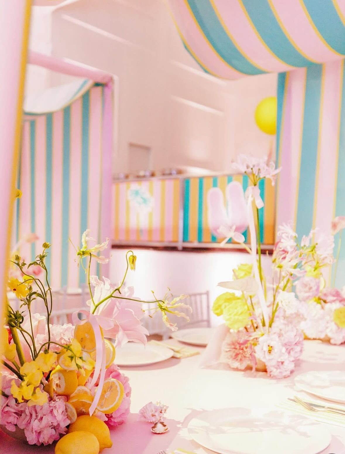 Floral centerpieces with lemons on a table with colorful striped fabric draping.