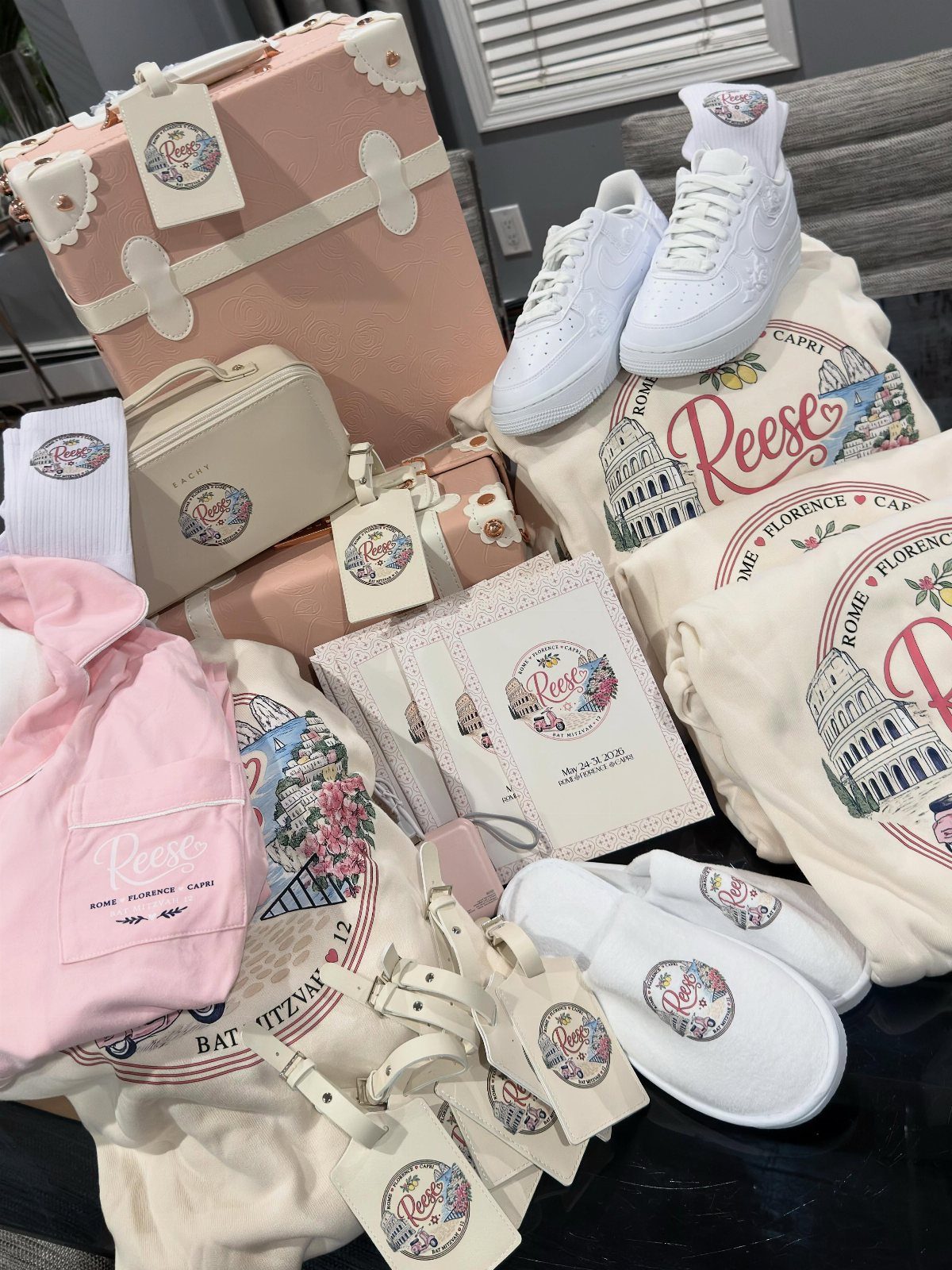 Travel-themed Bat Mitzvah party favors including a pink suitcase, white sneakers, and sweatshirts.