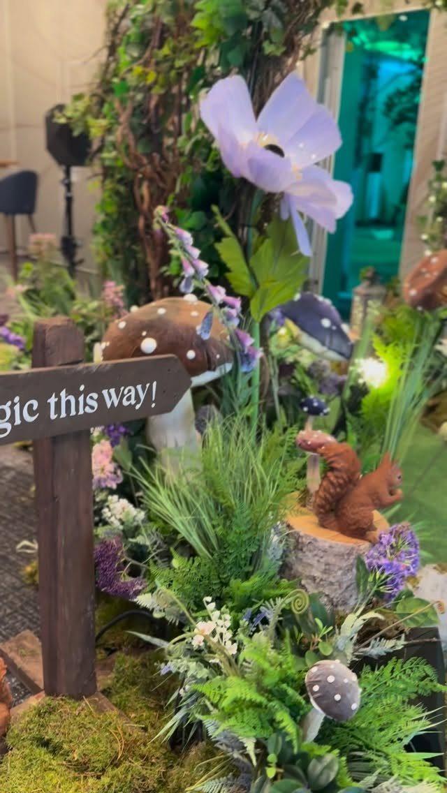 Whimsical forest decor with oversized mushrooms, purple flowers, and a wooden directional sign.