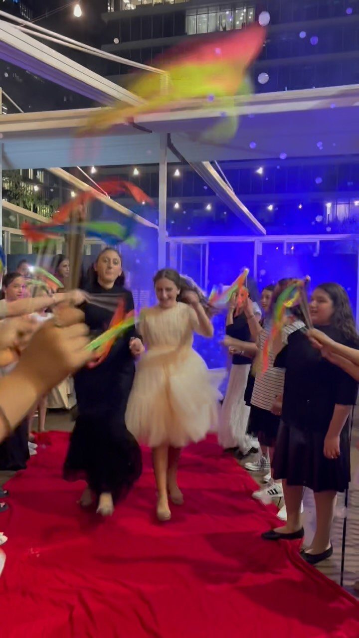 Girl in cream tulle dress walking red carpet with guests waving colorful ribbons