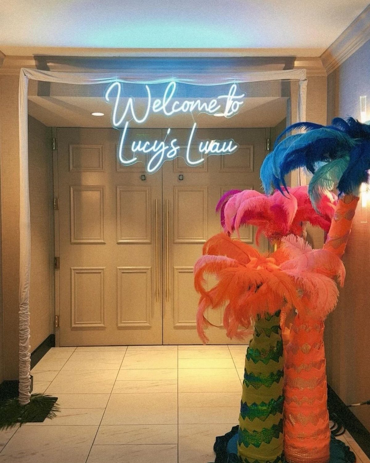 Neon welcome sign for Lucy's Luau with colorful feathered decorative palm trees