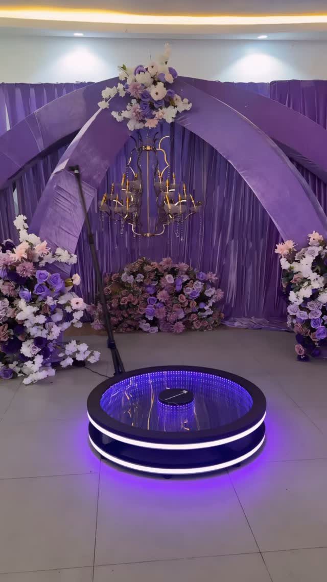 Circular 360 photo booth platform with purple lights against a purple floral backdrop.