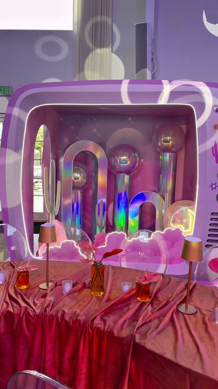 Purple photo booth with iridescent arches and balloons behind a red satin table.
