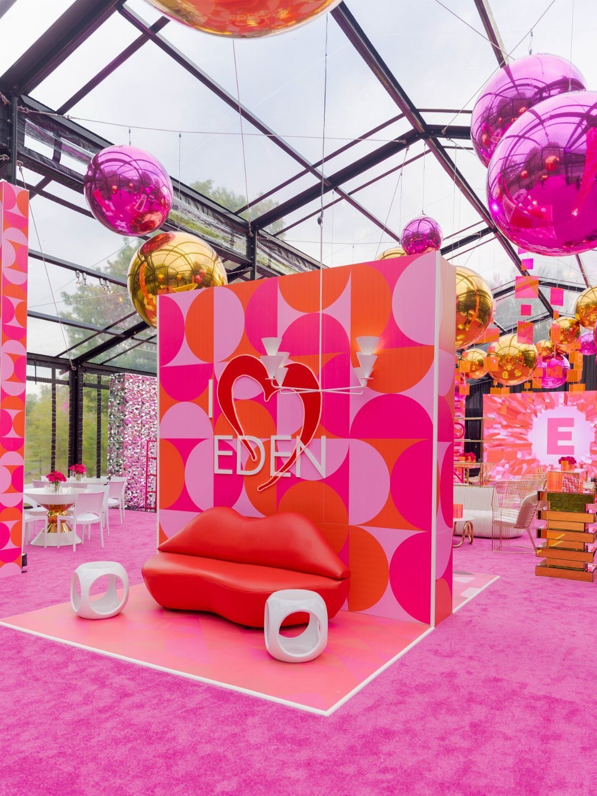 Vibrant event photo booth setup with red sofa and pink geometric backdrop.