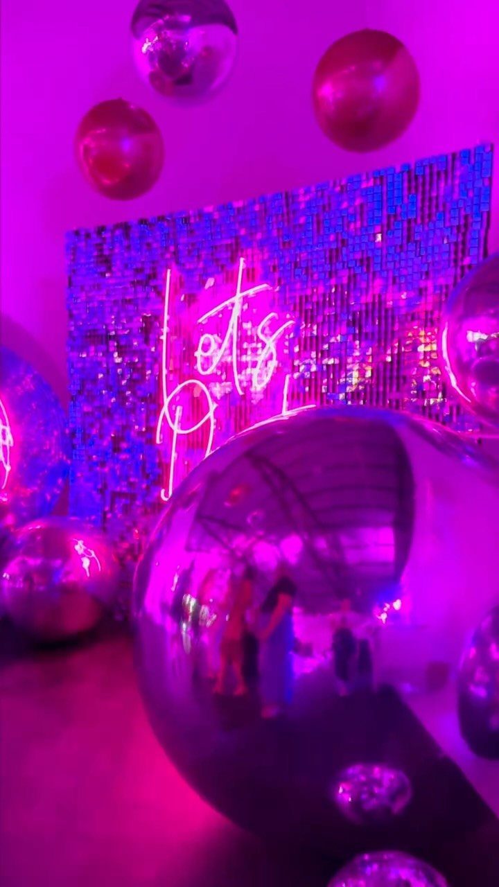 Shimmering blue sequin backdrop with neon sign and large silver disco balls.