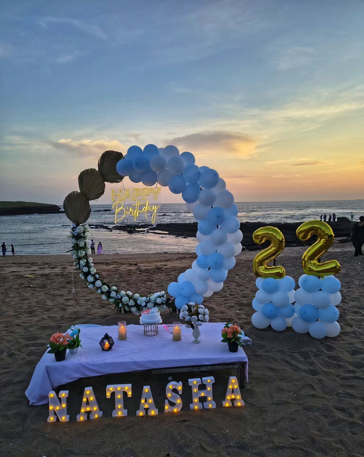 Circular blue and white balloon arch with gold numbers on a sandy beach.