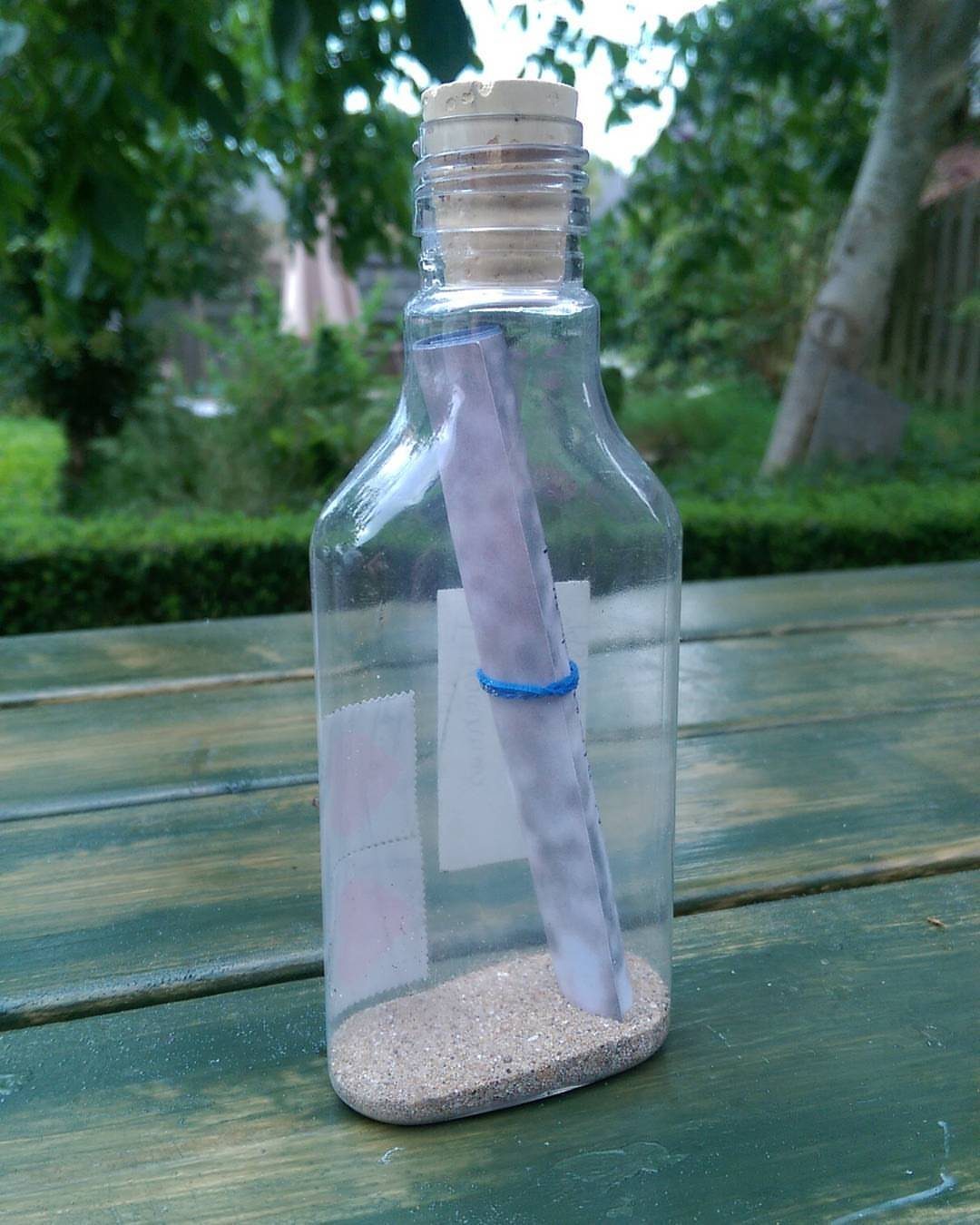 Small glass bottle with a rolled message, blue string, and sand on table.