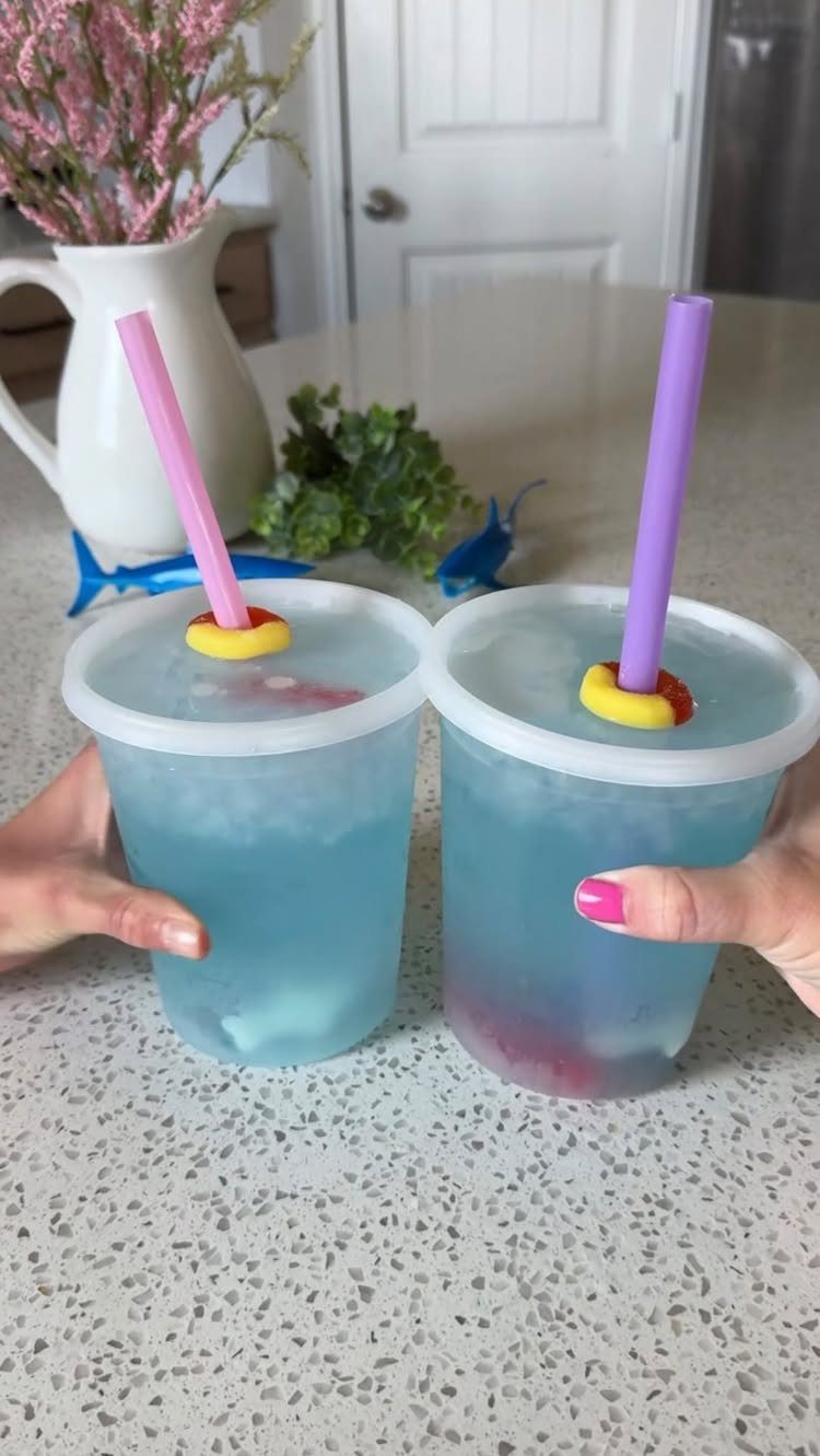 Two bright blue ocean water punch drinks in plastic cups with colorful straws.