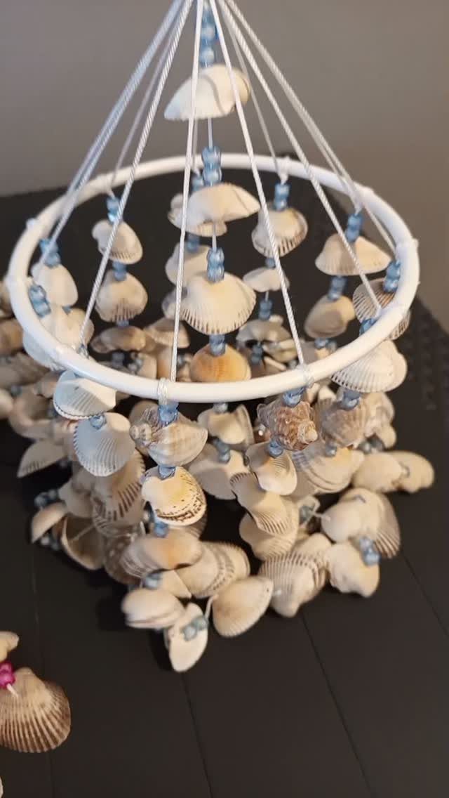 Handmade seashell wind chime with white hoop and blue beads on dark surface