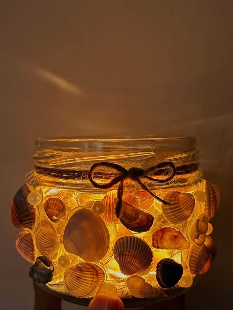Seashell decorated glass jar glowing with warm yellow light and tied with twine.