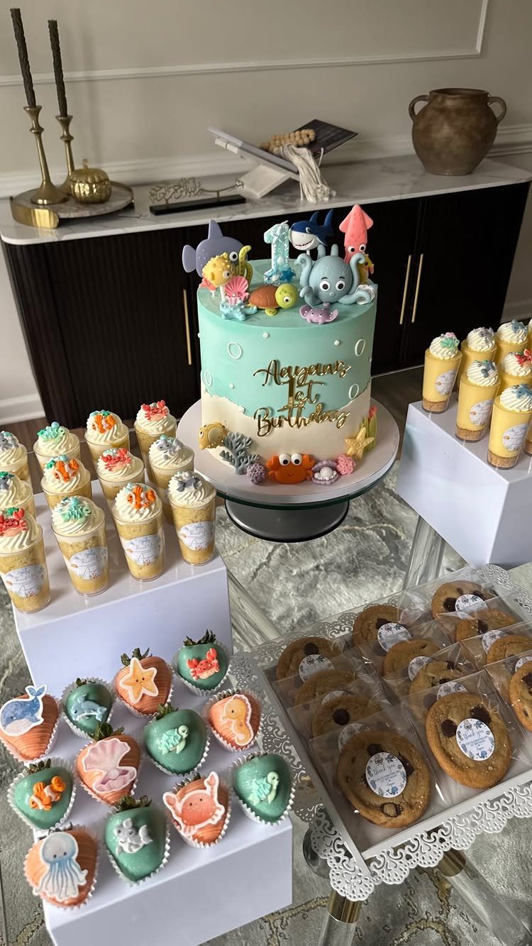 Under-the-sea cake with ocean animals surrounded by themed cupcakes and treats.