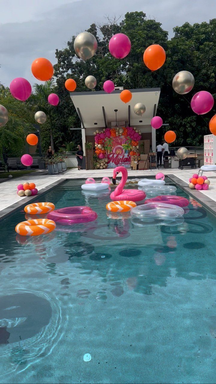 Swimming pool party decorations with colorful balloons and inflatable floats in blue water.