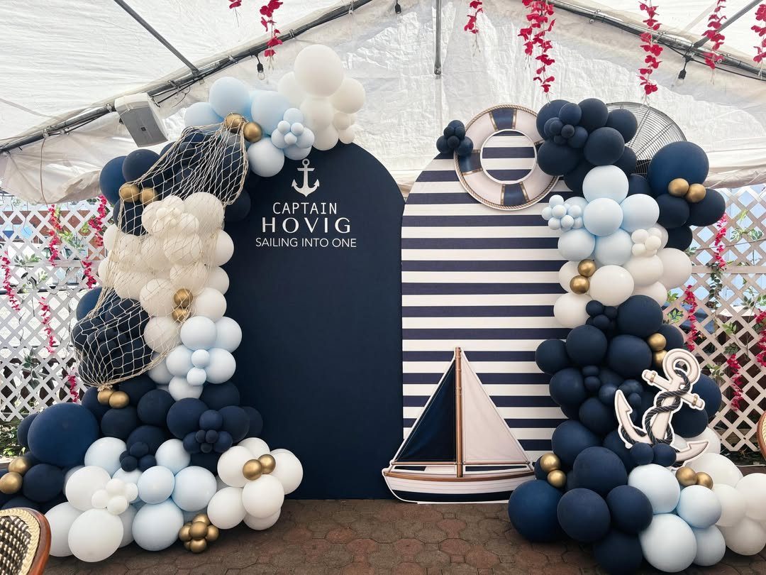 Nautical party decorations with navy and white balloons, a sailboat, and anchor backdrop.
