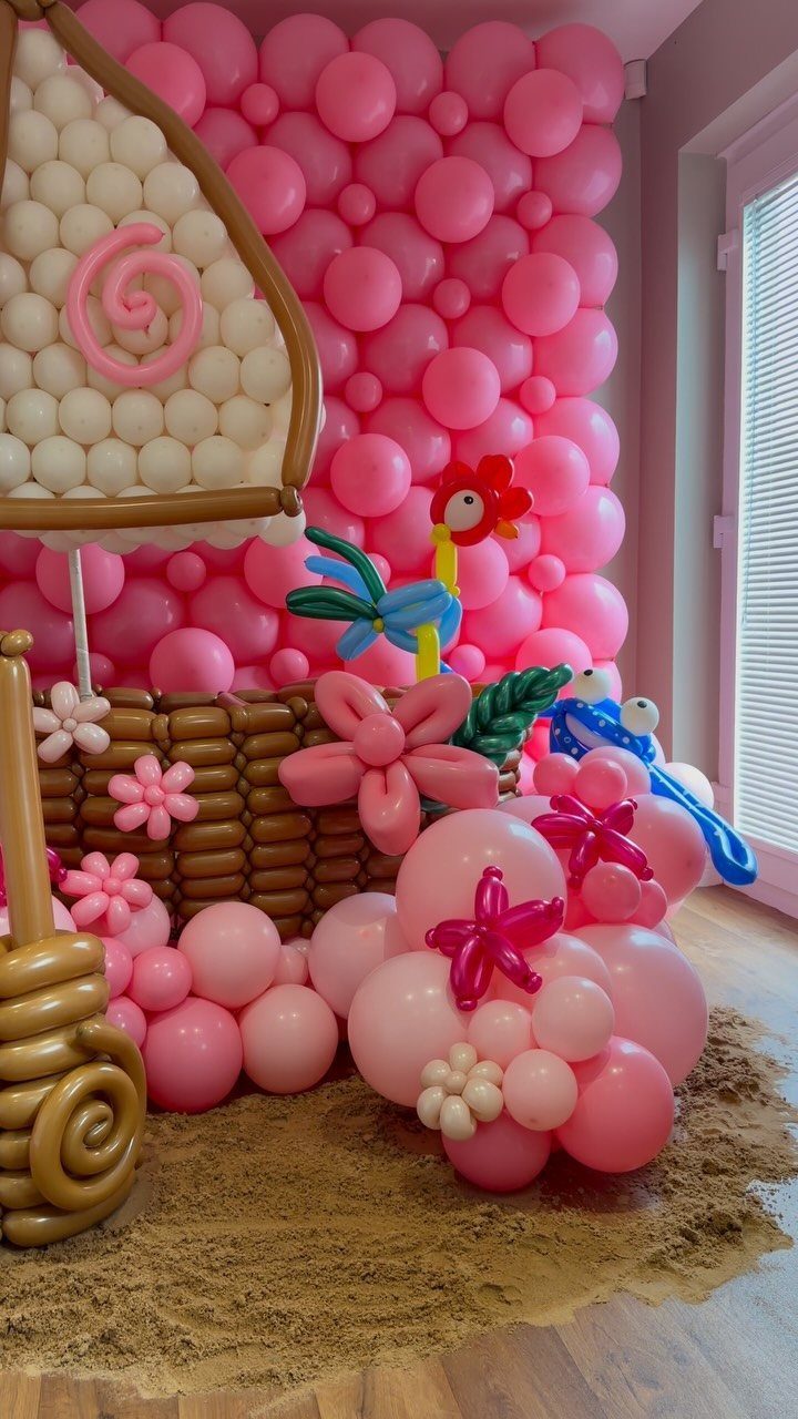 Pink and white balloon decorations with sand on the floor and a woven basket.