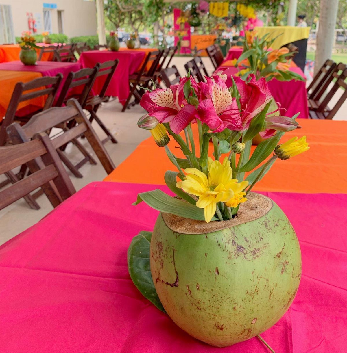 Tropical pink and yellow flowers arranged in a green coconut shell on a table.