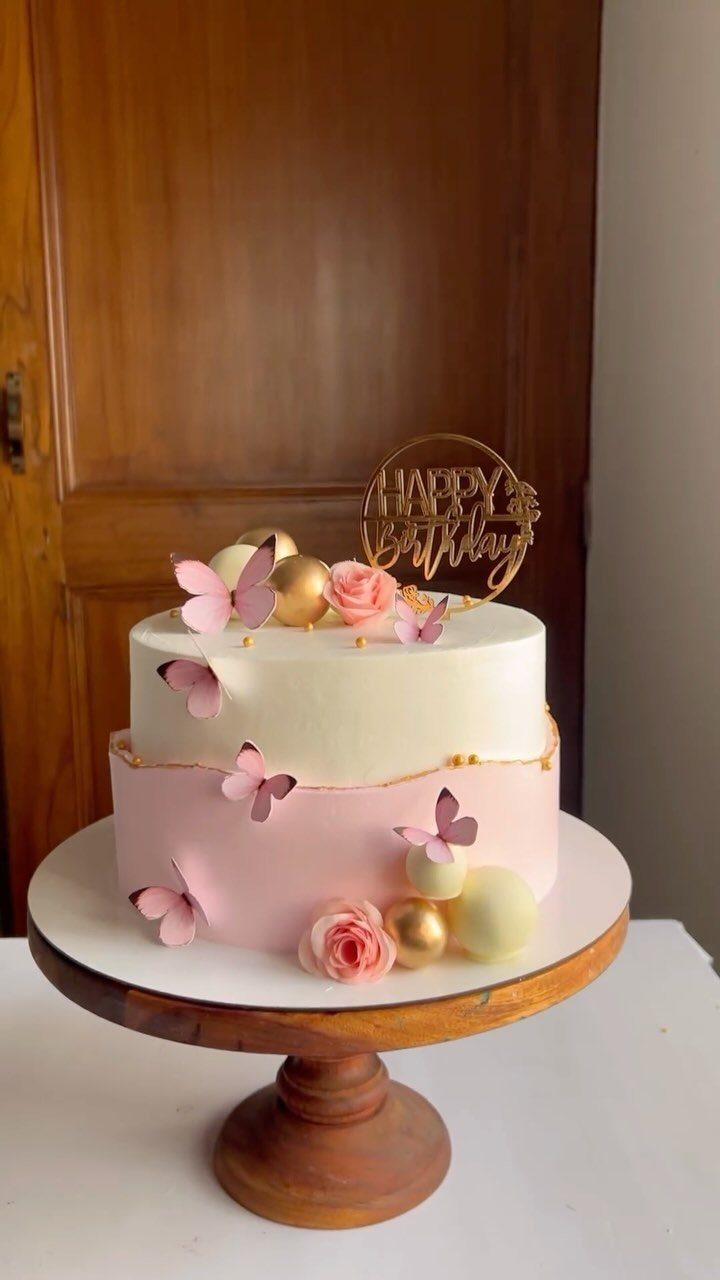 Two-tier white and pink birthday cake decorated with pink butterflies and gold spheres.