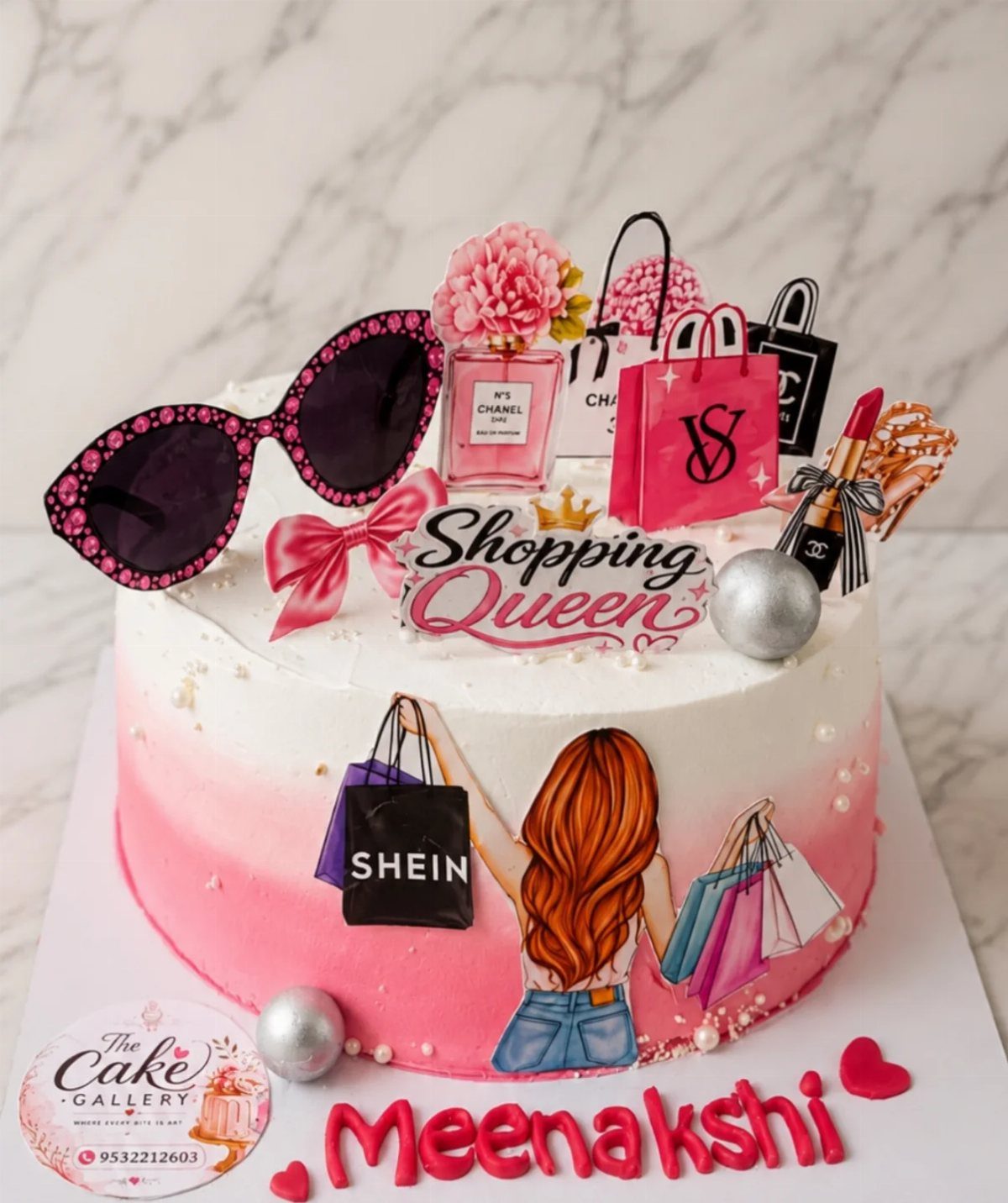 Pink and white ombre cake decorated with shopping bags, sunglasses, and accessories.