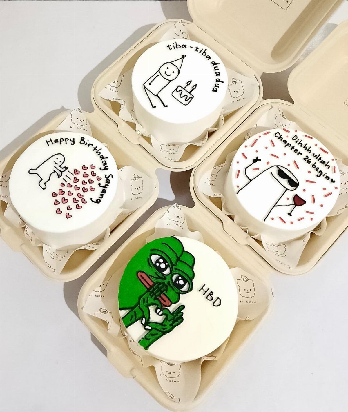 Four mini white bento cakes with cute drawings in small cardboard boxes.