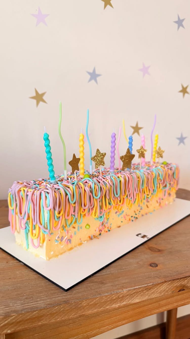 Yellow cake with colorful dripping frosting and multicolored spiral candles and gold stars.