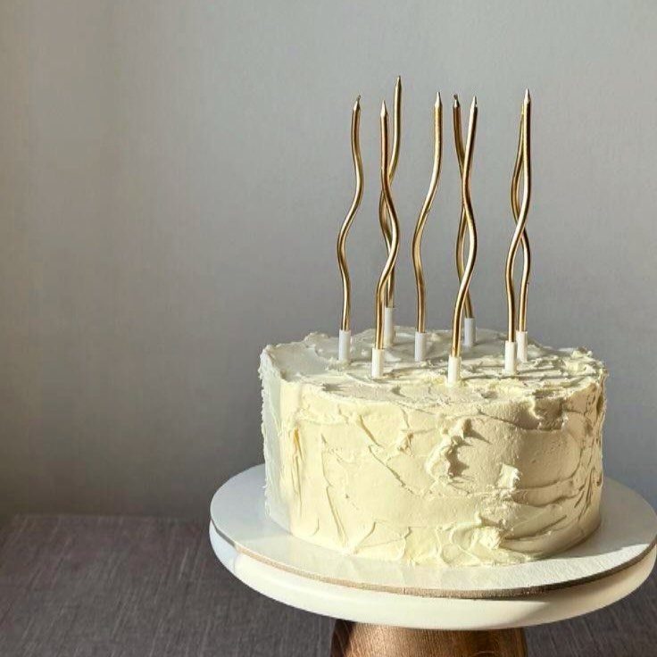 White frosted cake topped with tall thin gold wavy candles on a stand