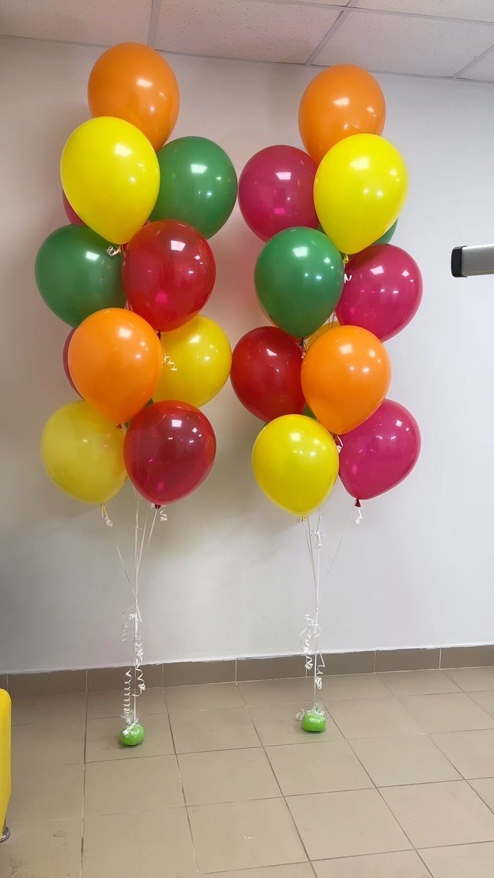 Colorful balloon clusters in red, yellow, green, and orange against a white wall.