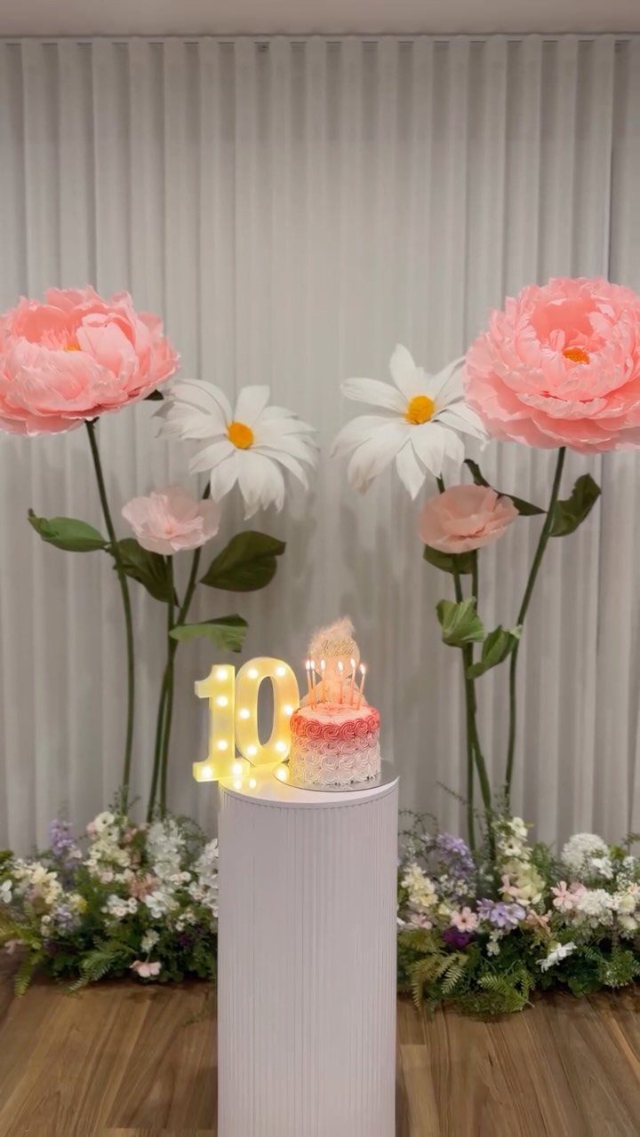 Large pink and white paper flowers decorating a birthday cake display with number 10.