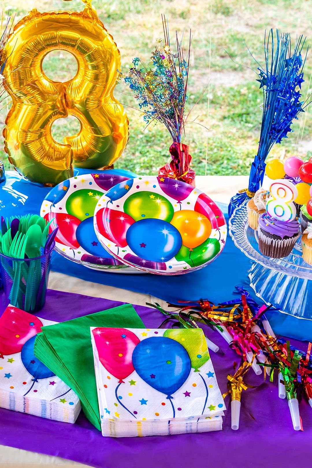 Gold number 8 balloon and colorful party supplies on a purple tablecloth.