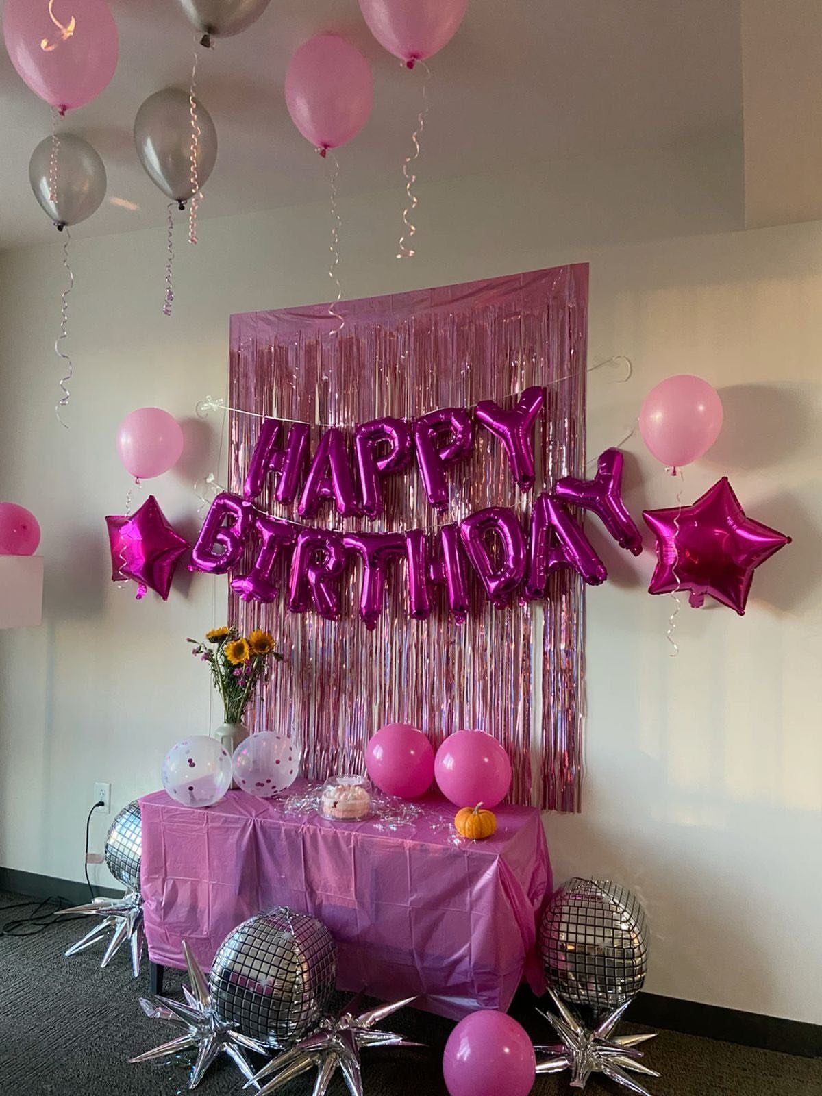Pink foil fringe curtain backdrop with Happy Birthday balloons and disco ball decorations.