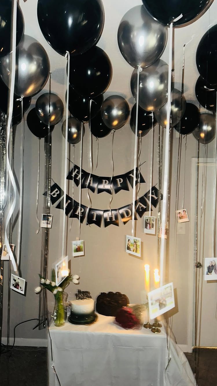Black and silver balloons floating above a birthday cake and banner setup.