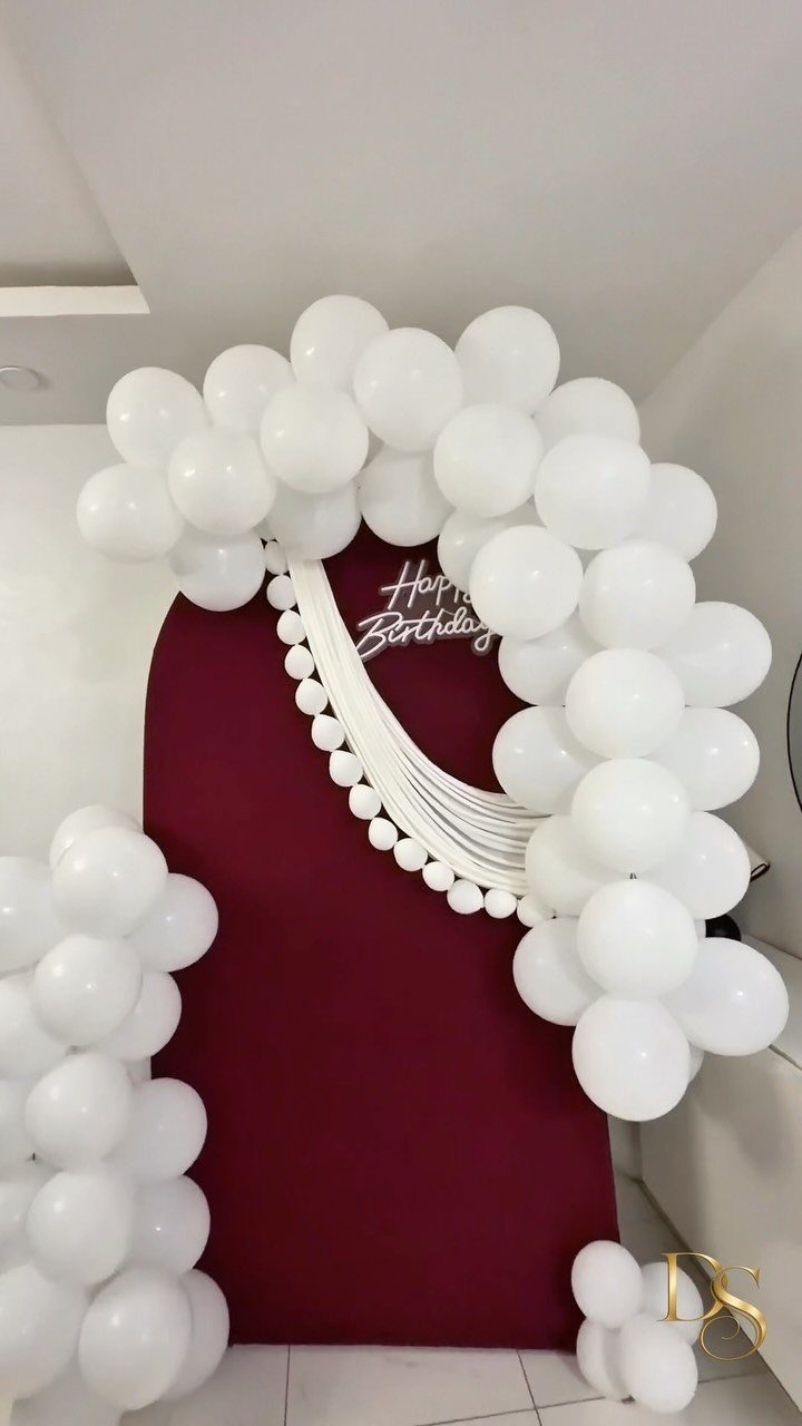 White balloon arch framing a red backdrop with Happy Birthday sign and strings