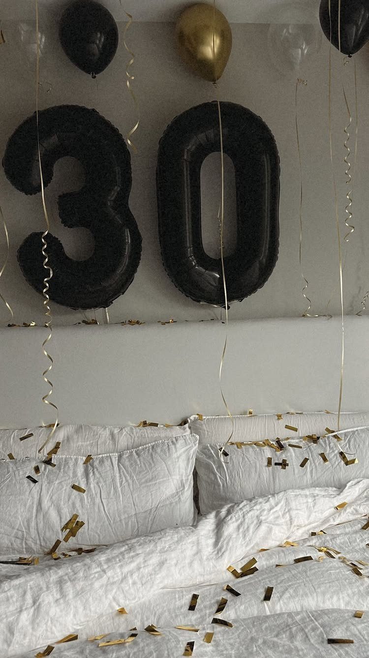 Black and gold balloons with number 30 above a bed with gold confetti
