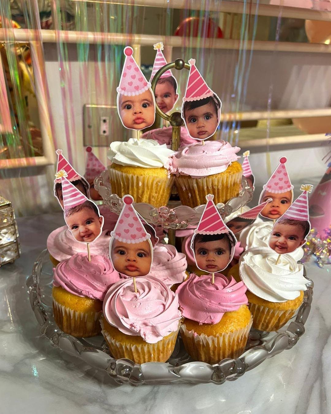 Cupcakes with pink and white frosting topped with customized baby face cake toppers.