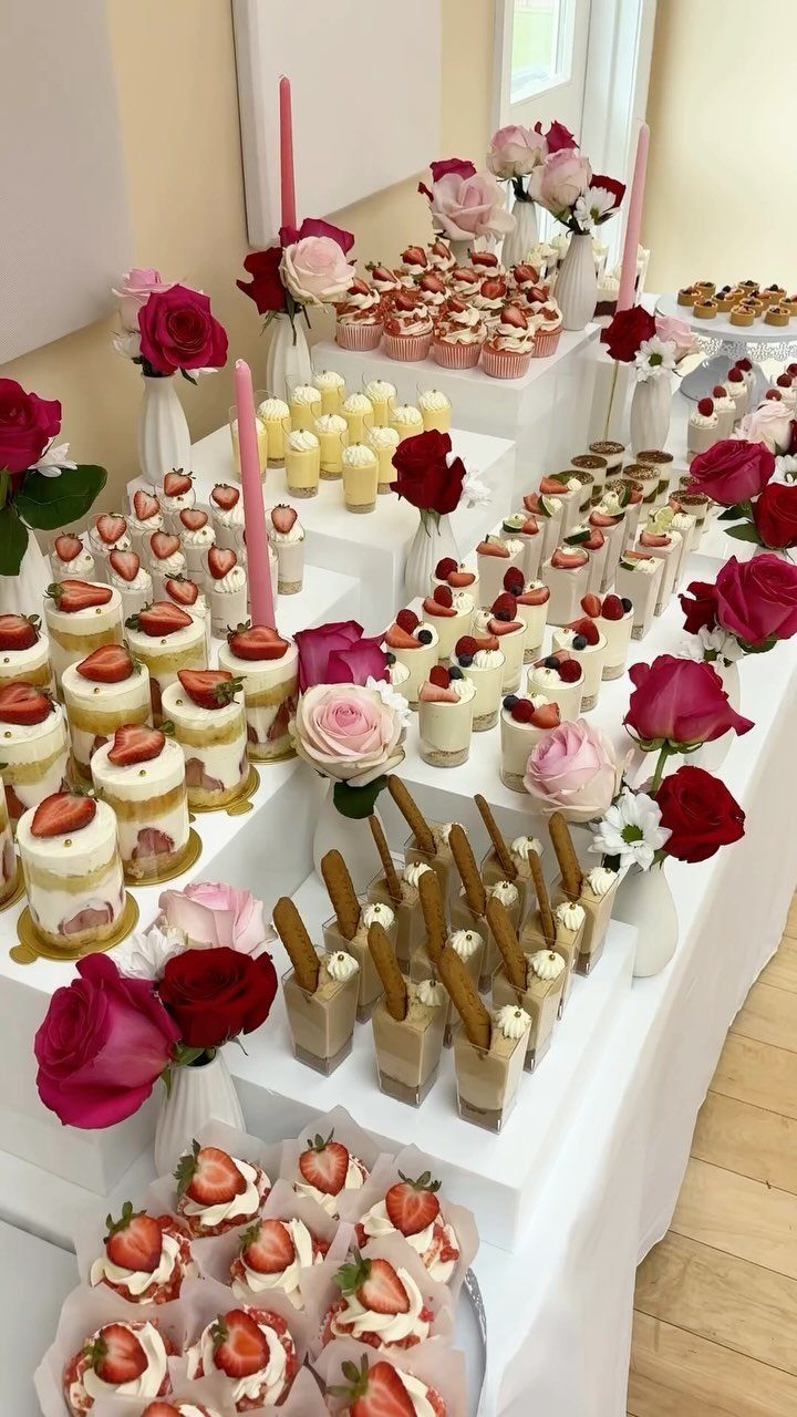 Dessert table display with strawberry cakes, cupcakes, and red and pink roses.