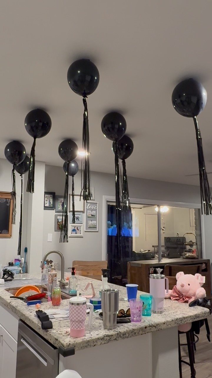 Black balloons with long tassels floating on a white ceiling in a kitchen